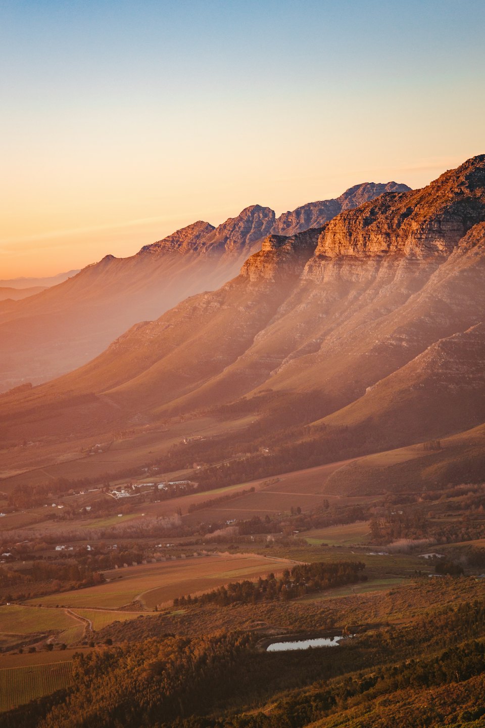 Golden sunrise over a hazy mountain range and valley fields.