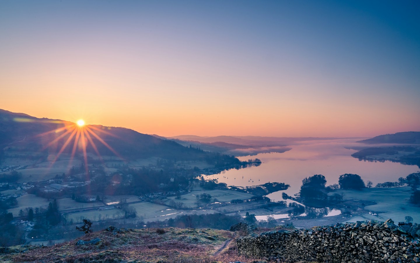 Sunrise over a misty valley and calm lake with golden rays.