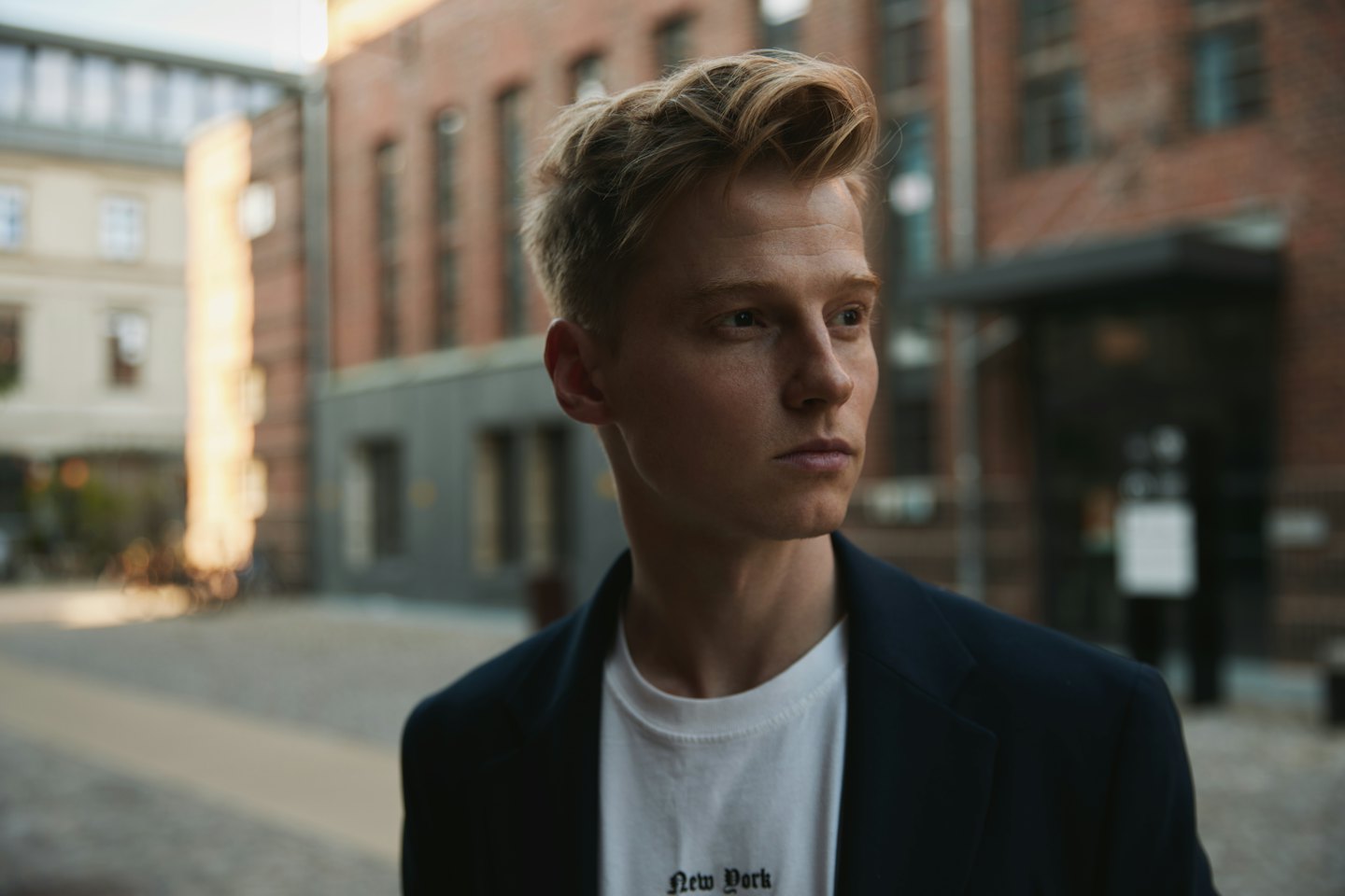 Man in a navy blazer stands on a city street.
